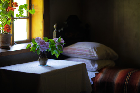 Vase with lilac flowers in the bed with pillows in the bedroom of an old houseの写真素材