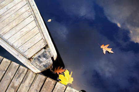 Nose of wooden boat at the dock of the boards and the leaves of autumn with reflection of blue skyの写真素材