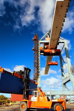 Yellow forklift and crane at unloading and loading cargo at the port on a background of blue skyの写真素材