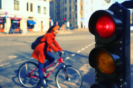 Girl in a red coat on a bicycle at the intersection of the city for a red traffic light in spring dayの写真素材
