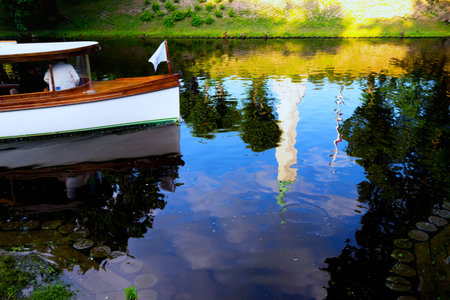 Latvia, Riga. July 2015. Tourists on a boat with a flag on a city canal with reflection Freedom Monumentのeditorial素材