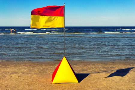Latvia. Yellow-red flag on a yellow sandy beaches of the Baltic Sea in the summer sunny day on a background of gray-blue skyの写真素材