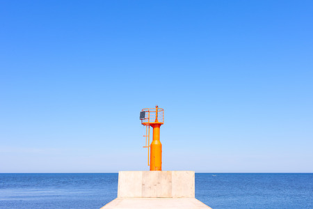 Baltic sea, Latvia. Modern orange beacon on a flat horizon against a blue sky with no clouds and the seaの写真素材