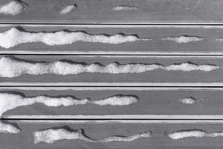 Snow melts on the boards in striped lines on the terrace of the house in spring