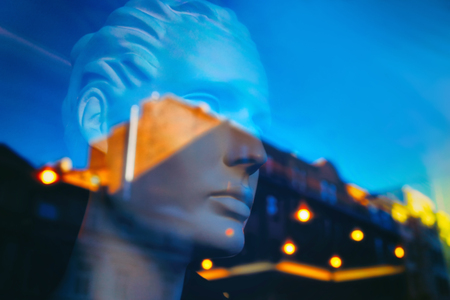 The sky and the lights of the city at sunset in reflection on the glass showcases with a mannequin head. Blurryの写真素材