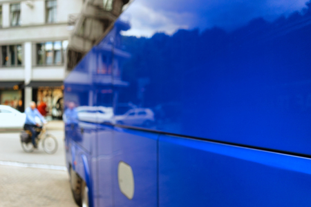 A cyclist rides down the street past the shop windows and the reflection of the city in the side of the blue bus. Blurryの写真素材
