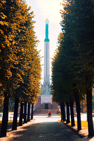 A view of the Freedom Monument in Riga in the autumn through the mall with cyclists on a sunny dayのeditorial素材