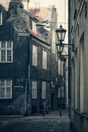 Motorcycle parked on the dark narrow streets of the old city of Riga with old houses and street lampsのeditorial素材