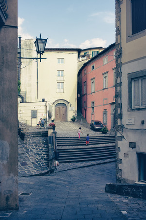 Children playing in the courtyard with stairs among the houses in a typical small town in Italyの写真素材