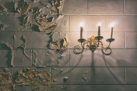Vintage gold light bulb burns on an old wall with traces of water stains painted on dirty wallの写真素材