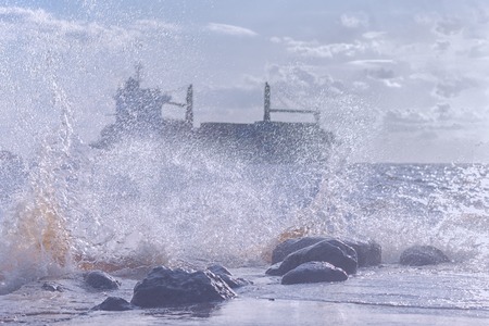 Silhouette of a commercial ship in a stormy Baltic sea through the spray of the waves on the rocks...