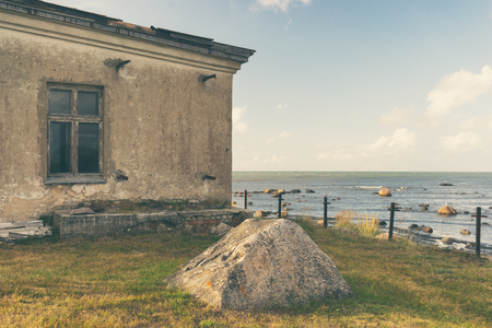 A stone fisherman's house on the shore of the Baltic Sea next to the Tahkuna lighthouse on the background of the horizonの写真素材