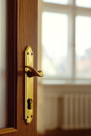 A wooden door with a yellow brass padlock is open to an empty room with windows and a radiatorの写真素材