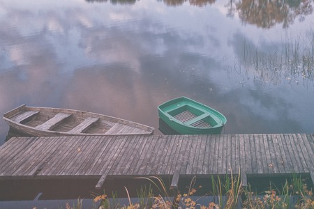 Two boats are tied to a wooden pier on the lake in the autumn evening with a reflection in the water of the cloudsの写真素材