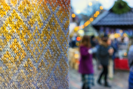 Woolen scarf with national Latvian ornament of yellow and gray threads on the background of the Christmas Fair in Rigaの写真素材
