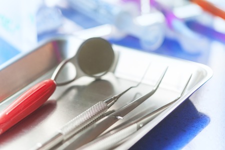 Dental tools and tweezers lie in a metal tray on the table. Blurryの写真素材