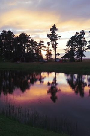 Sunset in camping with a purple reflection of clouds and pines in the lake waterの写真素材