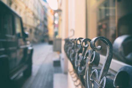 A black car is parked at the metal fence of a building on a narrow streetの写真素材