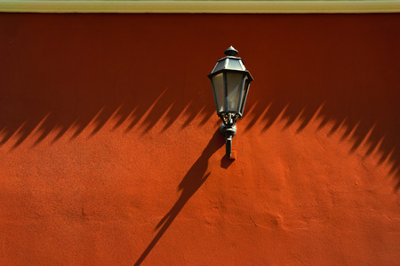 Street lamp on a painted red wall with long shadows in the old townの写真素材