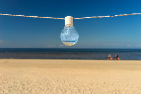 A bulb hanging on white on a wire on a sandy beach against a blue summer sky backgroundの写真素材