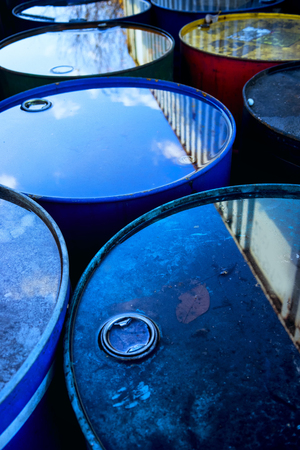 Reflection of blue sky and trees in the water on the lids of old barrels near a container on the...