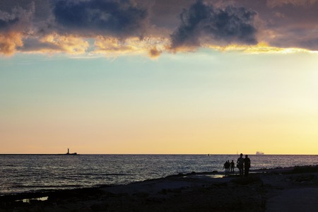 People go to the lighthouse at the mouth of the river to watch the sunset in the Baltic Sea