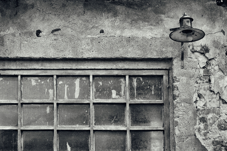 Old brick wall of the house with a lantern and a window in the paint on a black and white photoの写真素材