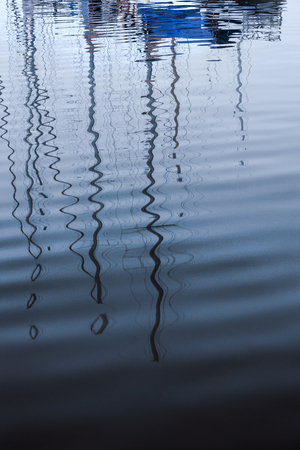 Masts with rigging without sails are reflected in the waves of the port bay