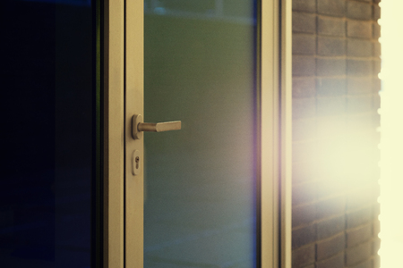 Metal handle on a closed glass door in the sunlight with highlights on a brick wallの写真素材