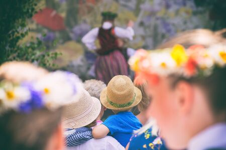Spectators in national costumes with wreaths of flowers on their heads watch a concert with dances at Ligo in Latviaの写真素材