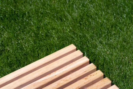 The corner of a wooden bench of light boards on the background of green grassの写真素材