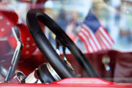 Saloon with leather steering wheel of a red vintage car with the USA flag in the window