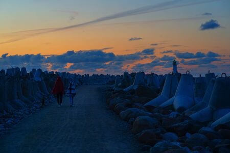 The couple goes on a romantic date to the sunset on the background of the concrete fortifications of the pier and the lighthouseの写真素材