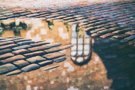 Reflection of a gothic window of a historic building in the water on a cobblestone bridge square after rain in Rigaの写真素材