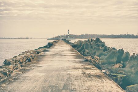 Couples walk on the pier with a lighthouse at the mouth of the Daugava River in the Gulf of Riga Baltic Sea. Riga, Latviaの写真素材