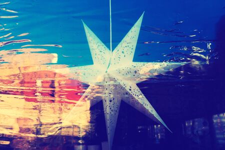 Paper star hanging on a window with reflection of buildings on the street and film on glass. Riga, Latviaの写真素材