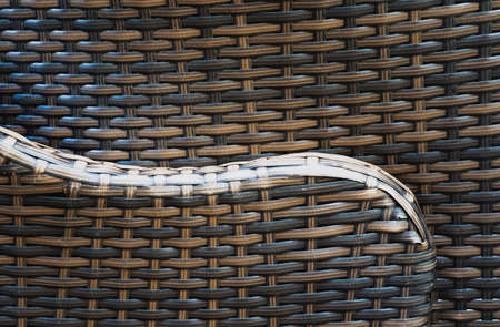 A graceful line of the arm of a rattan chair with embossed texture against the background of another chairの写真素材