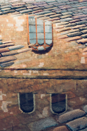 Reflection of the windows of an old house in the water on a cobbled street.の写真素材
