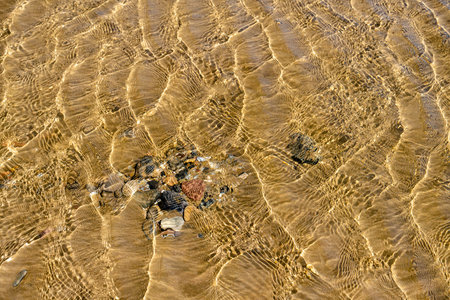 The stones lie on the yellow sand in the sea under clear water. The ripples from the waves are reflected on the bottom on a sunny day. Spainの写真素材