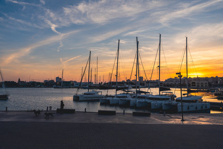 Yachts with reflection in the sea water of the port of Valencia. Port cranes on the horizon. Warm evening in Spain.の写真素材