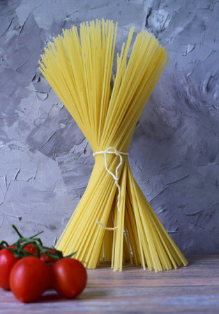 A bunch of spaghetti tied with a rope. a bunch of tomatoes set for a dish. vertically on a gray backgroundの写真素材