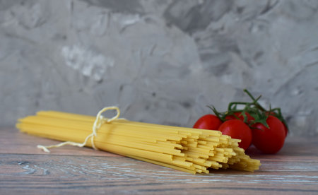 A bunch of spaghetti tied with a rope with a branch of cherry tomatoes, garizontal photoの写真素材