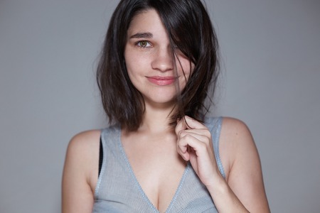 lovely beautiful young girl pulls a strand of hair, she looks at the frame, the picture is made in a light gray scaleの写真素材