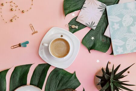 Office table desk. Tropical Flat lay. Home office workspace. Coffee cup and monstera leaf on pink background.の写真素材