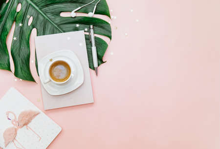 Top view women's office desk, workspace with coffee cup, monstera leaf on pink background.