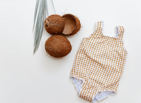Baby swimsuit and coconut on beige aground, minimal summer holiday composition flat layの写真素材