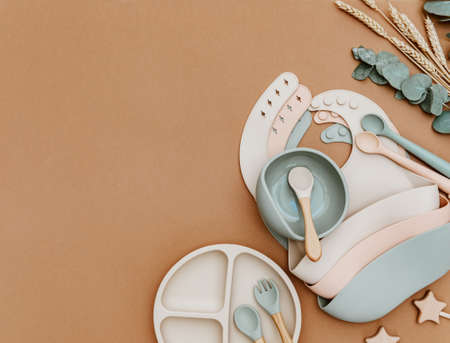 Composition with baby food accessory. Silicone cute dishware, bib and bowl on brown background. Neutral pastel colorsの写真素材