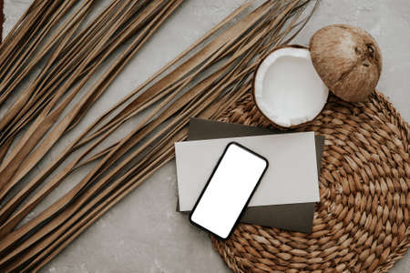 Summer stationery still life with blank phone, fresh coconut and dry palm leaves on stone background. stylish mock up with copy space on modern phone screen, social media mock upの写真素材