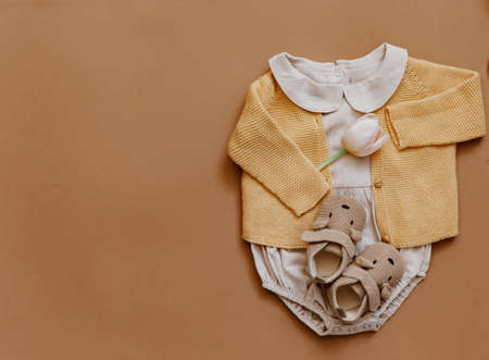 Baby clothes on brown background. Fashion baby outfit with tulips and booties. Top view, flat lay