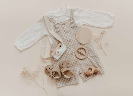 Flat lay Baby natural material accessories concept. Wooden toys, clothes and shoes on beige background. Bohemian baby fashion.の写真素材